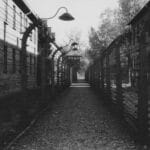 Czarno-biała droga w obozie koncentracyjnym otoczona drutem kolczastym