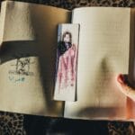 Dłonie trzymają otwartą książkę z artystyczną zakładką w słońcu