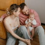 Rodzina z małym dzieckiem siedzi uśmiechnięta na sofie w przytulnym salonie