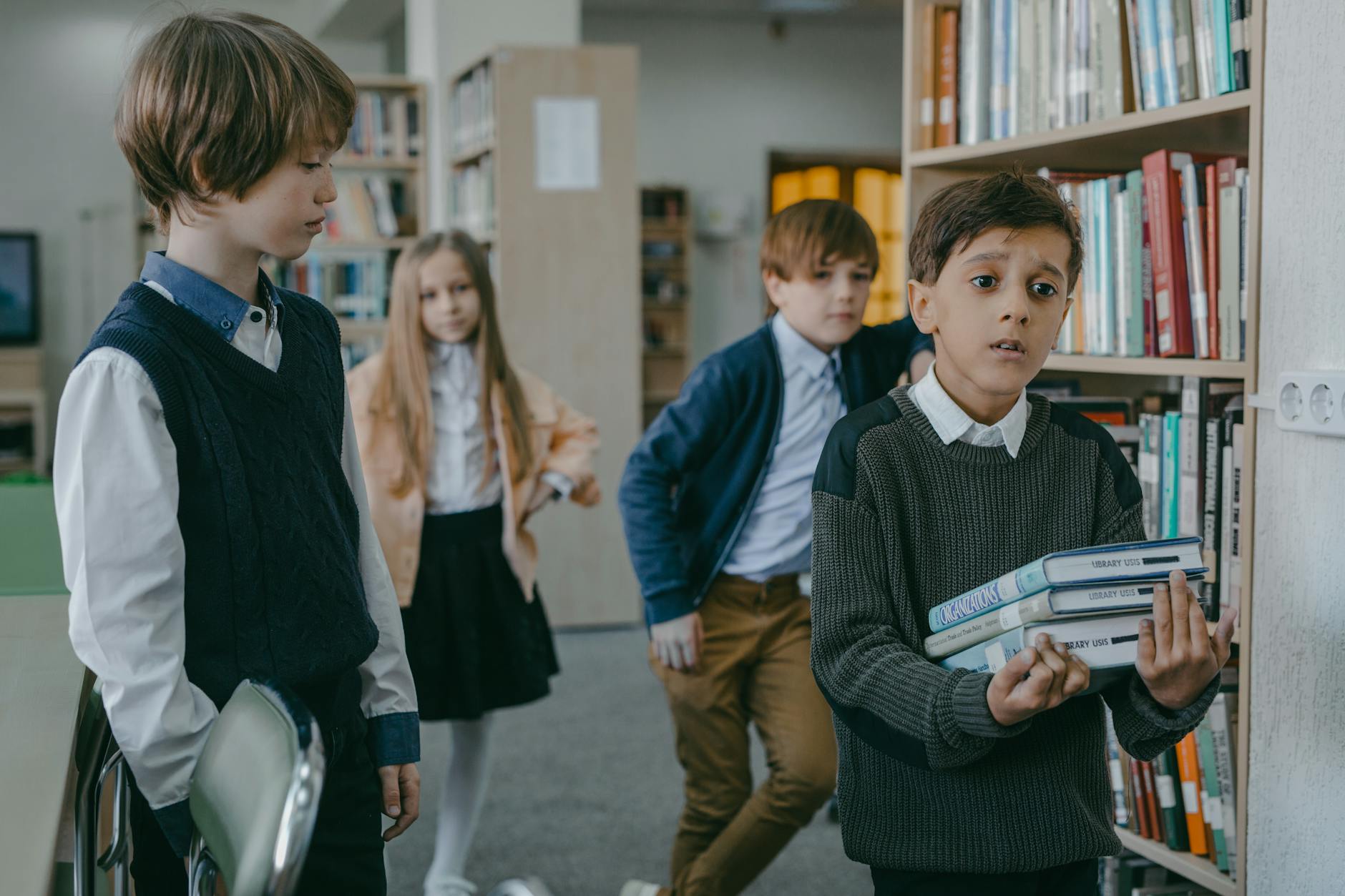 Chłopiec z książkami w bibliotece rozmawia z innymi dziećmi