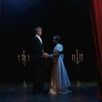 Dwójka eleganckich aktorów na scenie dramatycznego spektaklu przy świecach