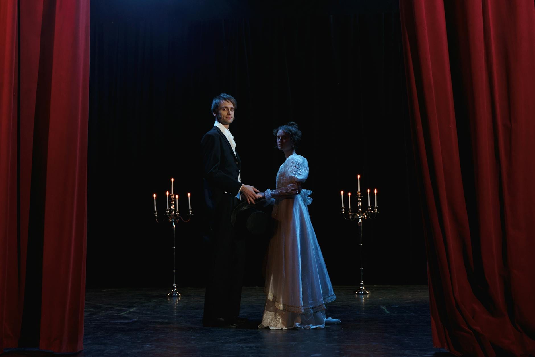 Dwójka eleganckich aktorów na scenie dramatycznego spektaklu przy świecach