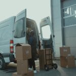 Kurier ładuje kartony do dostawczego busa pod magazynem