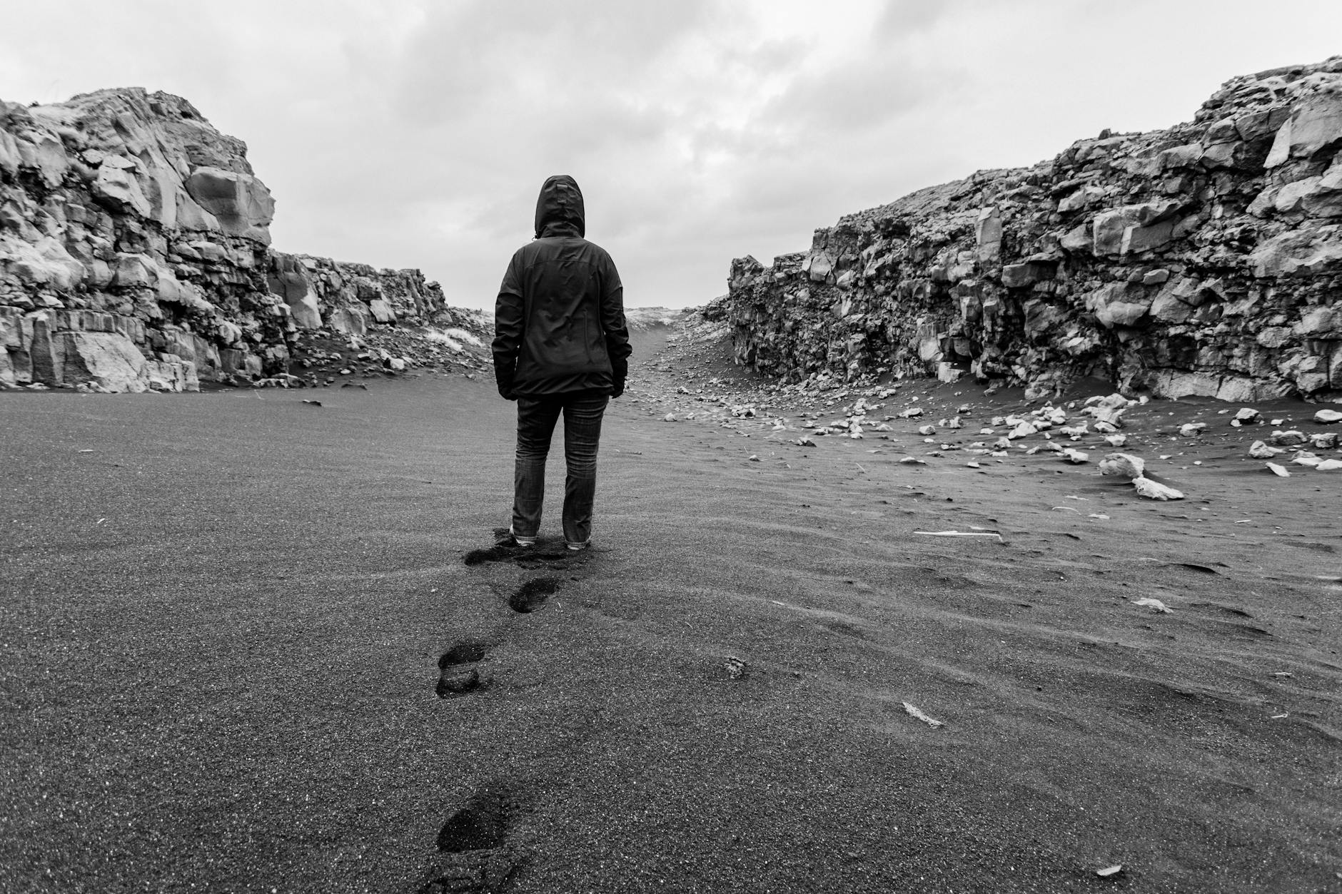 Postać w kapturze idzie po pustynnym, skalistym krajobrazie