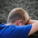 Smutny chłopiec w niebieskiej koszuli opiera głowę na ramionach na dworze
