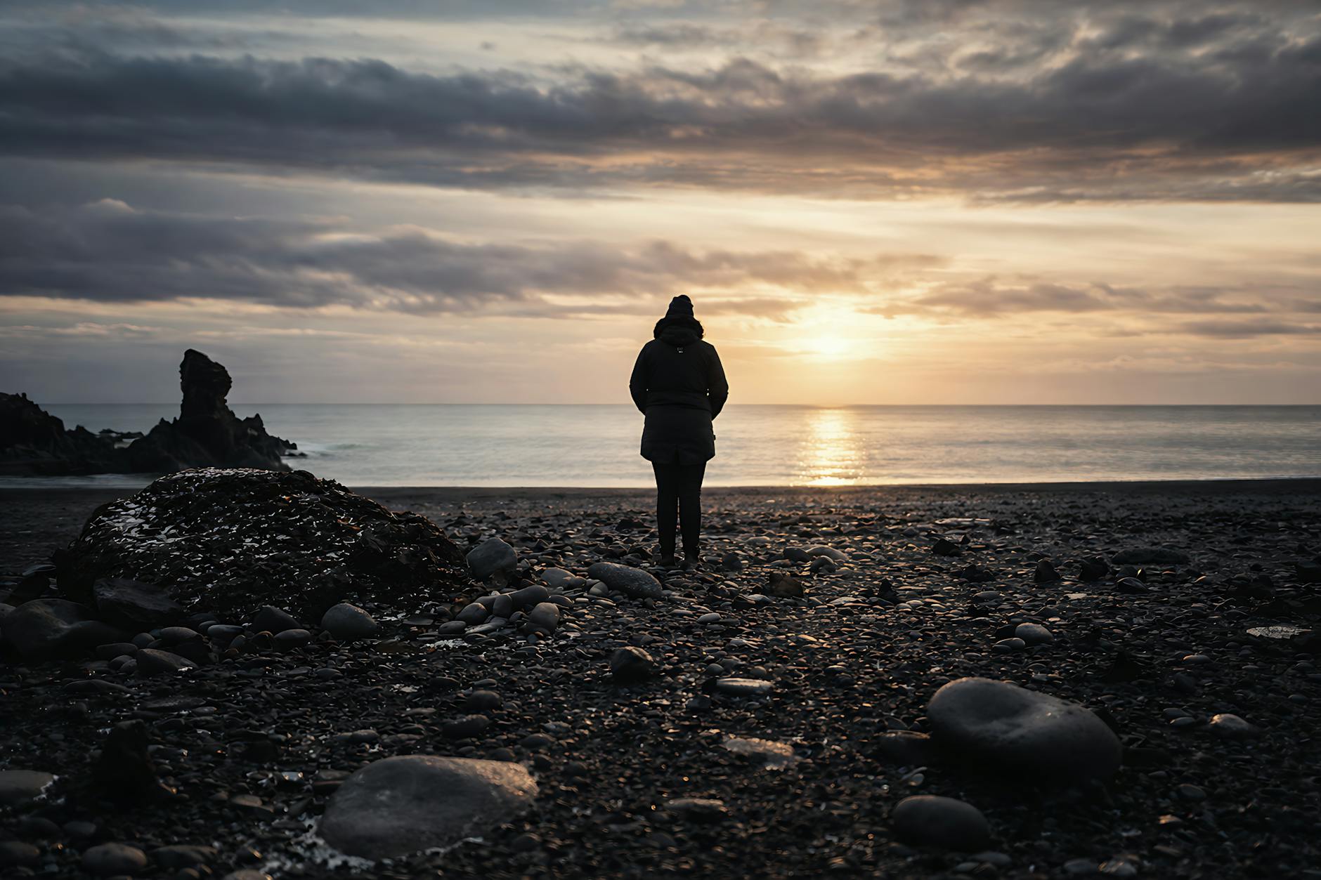 Sylwetka samotnej osoby na skalistej plaży o zachodzie słońca
