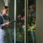 Kwiaciarka w fartuchu korzysta z tabletu przy ladzie z kwiatami